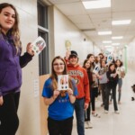 A group of young students hold up their hand drawn moose track stickers.
