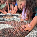 Children place their hands on a mosaic.