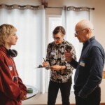 A teenager talks to two seniors who are taking notes.