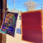 Two abstract paintings hang on a line in a window.