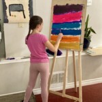 A child pains bands of colour on a easel.