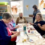 Women paint and talk around a table.