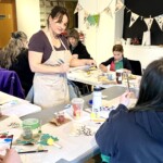 A woman stands and talks to people making art.