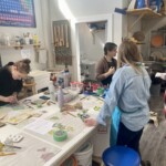 A group of people paint and listen to someone speak.