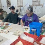 Two people paint on a paper covered table.